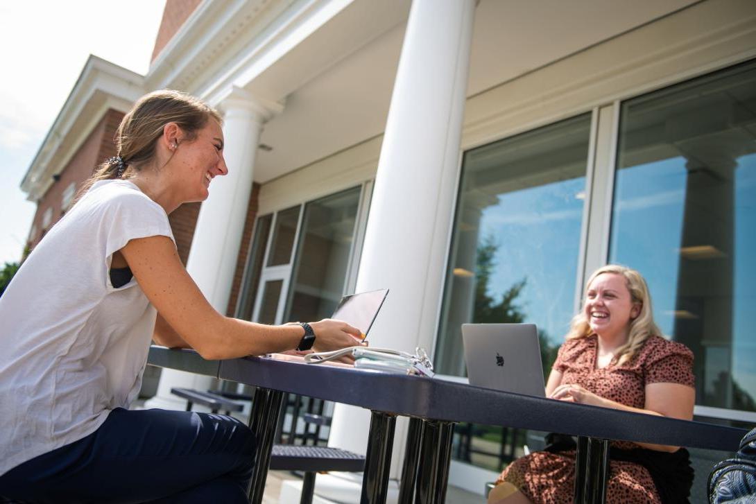 Photo of two students using computers outdoors